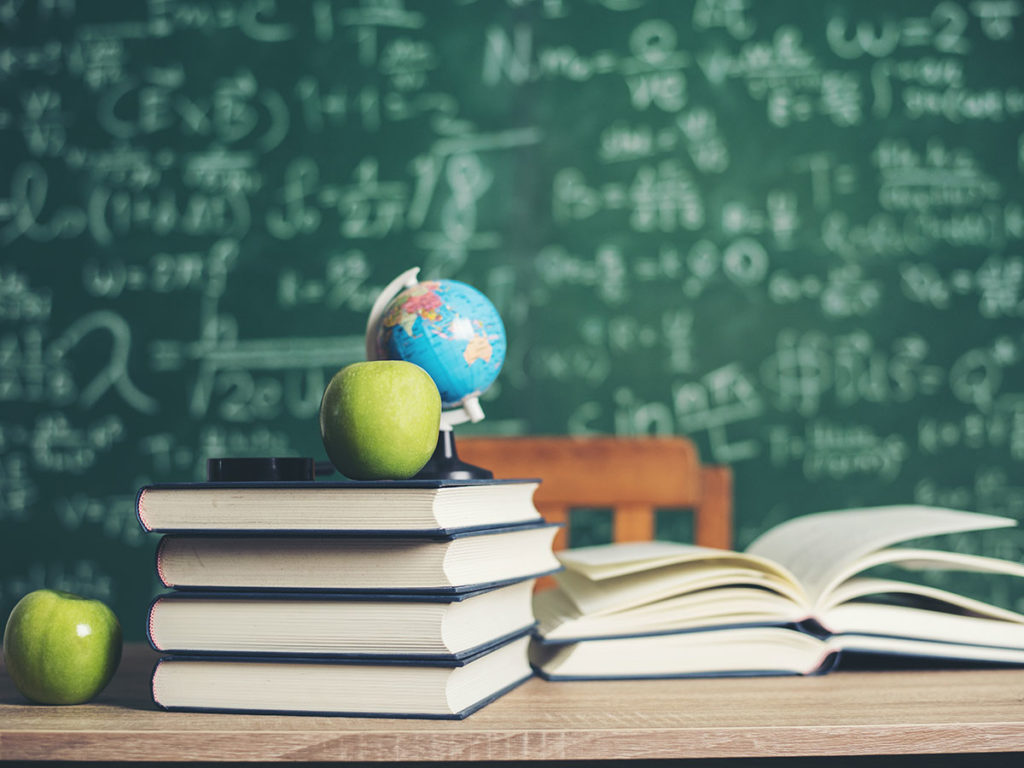 "Stack of books with a small globe on top, set in front of a chalkboard with equations."