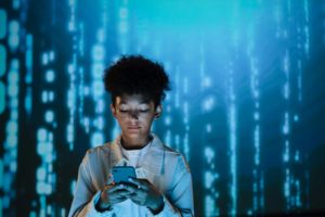 A young boy engaged with a cell phone, standing in front of a vibrant digital image.