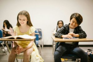 Two children engaged at their desks in a classroom, surrounded by educational materials and a bright learning environment.