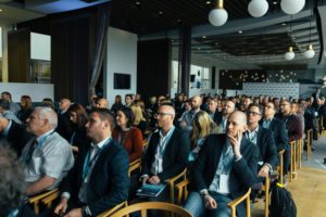A large crowd of attendees seated in chairs, engaged in a conference setting.