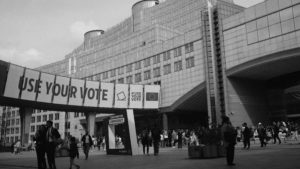 Black and white photograph featuring individuals walking in front of a prominent building, highlighting daily urban activity.