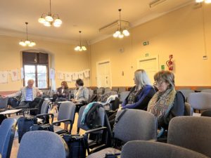 A group of people seated in chairs, engaged in conversation within a well-lit room.