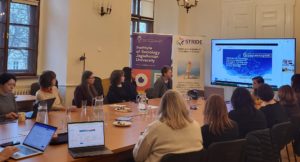 Workshop setting wehre people are sitting around a table and listening to a presentation about the STRIDE project