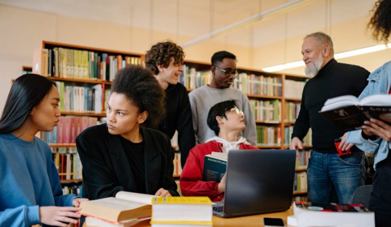 diverse learning environment with people gathered around a table with laptops and papers