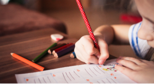 A child is writing on a piece of paper with a pencil.