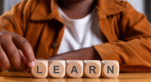 A person arranging wooden blocks that spell the word “LEARN” on a table.